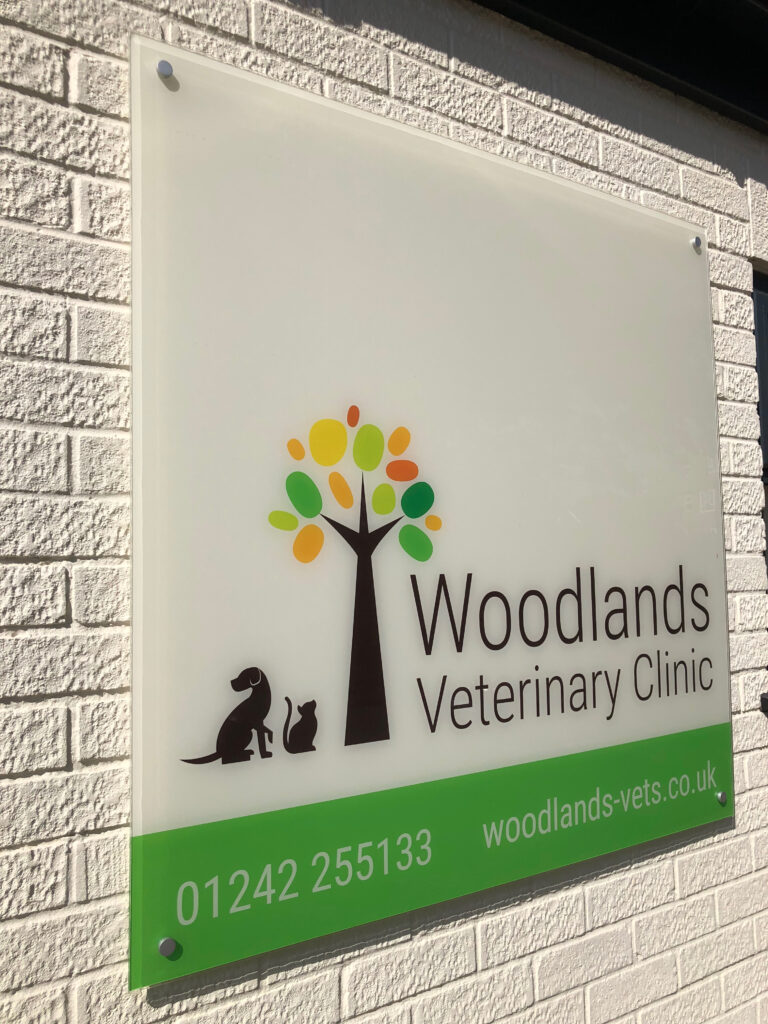 Acrylic sign for Woodlands Veterinary Clinic on a white brick wall